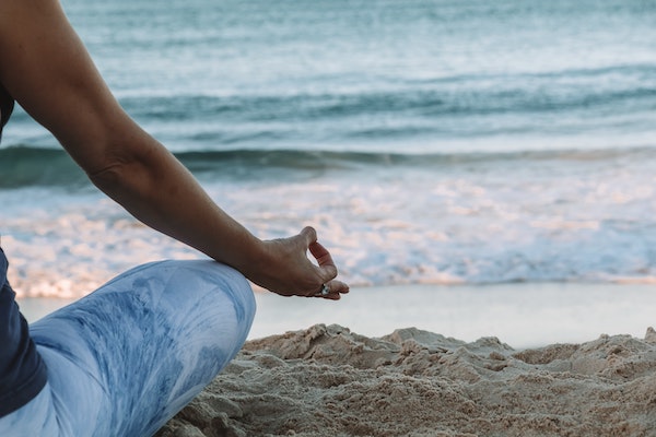 a woman meditating in front of the ocean on the beach sand